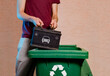 Man throwing old empty car battery in garbage disposal with recycling symbol 