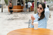 © PR Image Factory - fashionable asian Chinese businesswoman sitting with coffee using cellphone at food truck outdoor dining area during breaktime on city street in los angeles usa