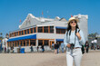 © PR Image Factory - leisure stylish asian Korean woman visitor exploring santa monica beach with camera on sunny day with a large local seafood restaurant at background