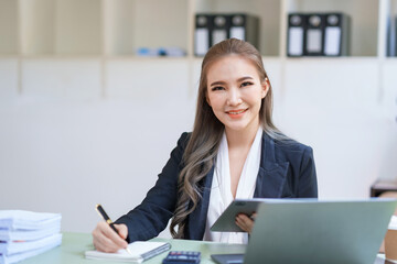 Wall Mural - Attractive Asian businesswoman with laptop in office With a bright smile and looking at the camera.