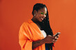 Vibrant, tech-savvy woman with dreadlocks smiles and uses her smartphone to browse the internet in a casual studio setting.