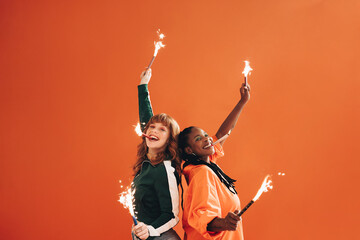 Pair of smiling, fun-loving friends celebrate and have a blast with sparklers and bengal lights in a party-ready studio setting