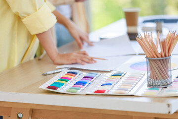 Closeup shot of colorful thread pattern collection placed on working table while unrecognizable professional dressmaker designer seamstress talking discussing together with colleague in tailor studio