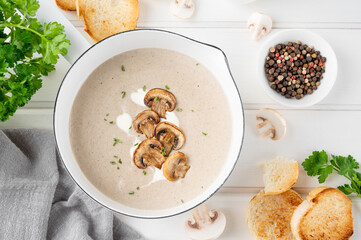 Wall Mural - Mushroom cream soup with cream, croutons and herbs on a white wooden background. Delicious comfort food.