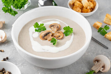 Wall Mural - Mushroom cream soup with cream, croutons and herbs on a white wooden background. Delicious comfort food.