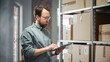© Gorodenkoff - Portrait of a Successful Employee Checking Inventory, Writing in Tablet Computer. Stylish Man Working in a Warehouse Storeroom with Rows of Shelves Full of Packages with Orders Ready for Shipment.