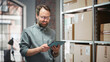 © Gorodenkoff - Portrait of a Happy Small Warehouse Employee Checking Inventory, Using Tablet. Handsome Man with Moustache Smiling in a Storeroom with Parcels and Online Purchased Orders Ready for Shipment.