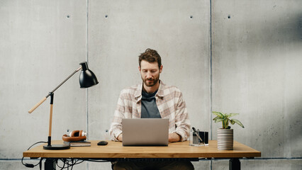 Aufkleber - Professional Creative Man Sitting at His Desk in Office Working on a Laptop Computer. Stylish Clean Office Space Design Perfect for Productivity, Effectiveness and Vision. Medium Shot