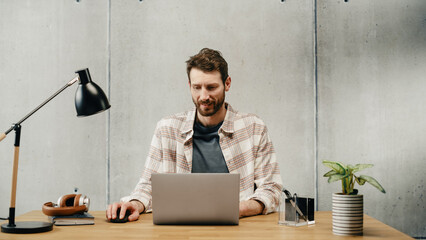 Aufkleber - Professional Creative Man Sitting at His Desk in Office Working on a Laptop Computer. Stylish Clean Office Space Design Perfect for Productivity, Effectiveness and Vision. Medium Shot