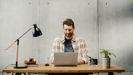 Aufkleber - Professional Creative Man Sitting at His Desk in Office Working on a Laptop Computer. Stylish Office Space Design Perfect for Productive Businessman Works on e-Commerce Project.