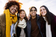 © Xavier Lorenzo - Portrait of four multiracial student friends in winter clothes smiling at camera. Millennial united diverse people standing together outdoors