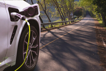 Wall Mural - In the background, an electric vehicle charging station is seen on an asphalt road. Concept for green alternative energy