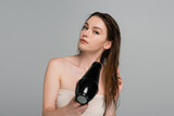 pretty young woman with bare shoulders and wet hair using hair dryer isolated on grey