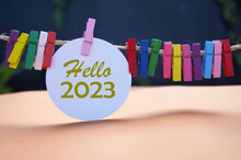 Hello 2023. New Year 2023 Concept With Golden Text On White Circle Paper And Colorful Wooden Clips On Rope On Dark And Light Orange Background. Fresh Hello 2023. Happy New Year.