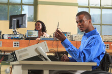 Engineering students in an electronics classroom, one in a wheelchair examining an oscilloscope probe