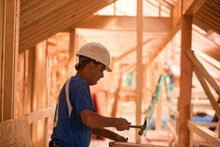 Hispanic carpenter hammering nails on board at a house under construction
