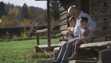 Childhood At Countryside, Kids With Grandfather Sit Together On Wooden Porch