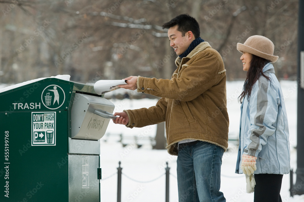 Young man throwing garbage into a garbage bin with a young woman standing behind him