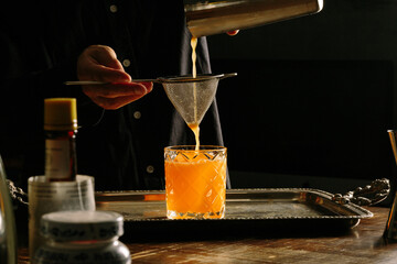 Wall Mural - male bartender pouring a cocktail with a cocktail shaker straining into a rocks glass