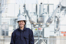 Portrait Of Female Power Engineer In Front Of High Voltage Transformer At Power Station