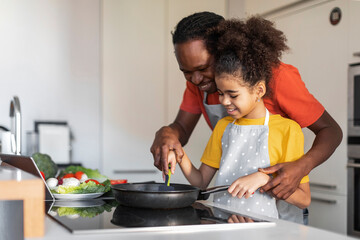 Cooking Time. Happy black dad and preteen daughter preparing lunch in kitchen