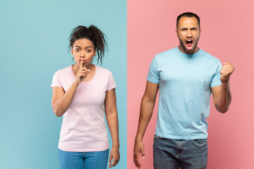 Young black woman gesturing hush sign, holding finger near mouth, man screaming and clenching fist at camera