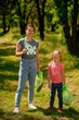 © Oleksandr - Blonde girl with eco symbol and her mom gathering garbage in the park
