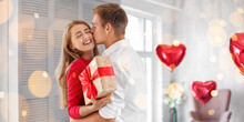 Young Couple With Gift For Valentine's Day Hugging At Home