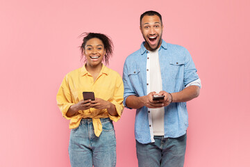 Mobile offer. Portrait of overjoyed black couple holding smartphones and looking at camera with excitement