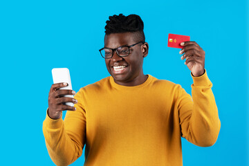 Wall Mural - Cheerful Young Black Man Using Smartphone And Credit Card For Online Shopping