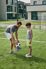 Vertical side view portrait of loving father teaching son football in outdoor court