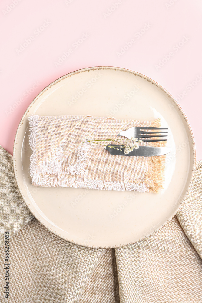 Plate with cutlery and napkin on pink background