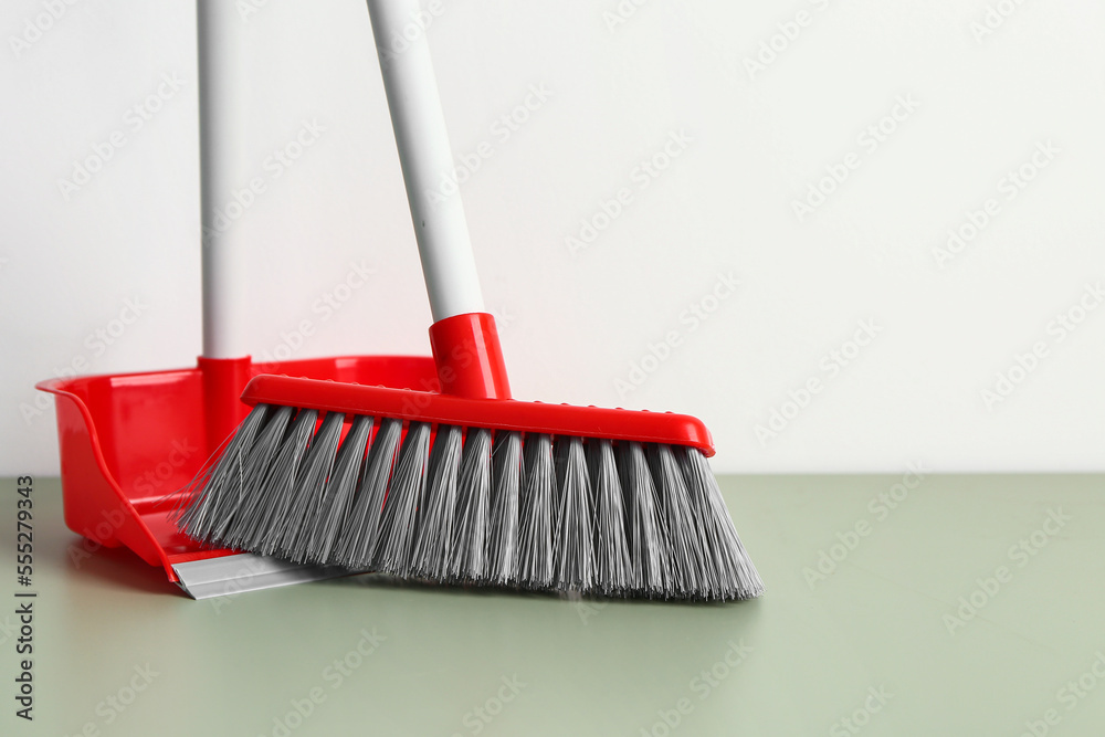 Dustpan and broom on floor near light wall, closeup