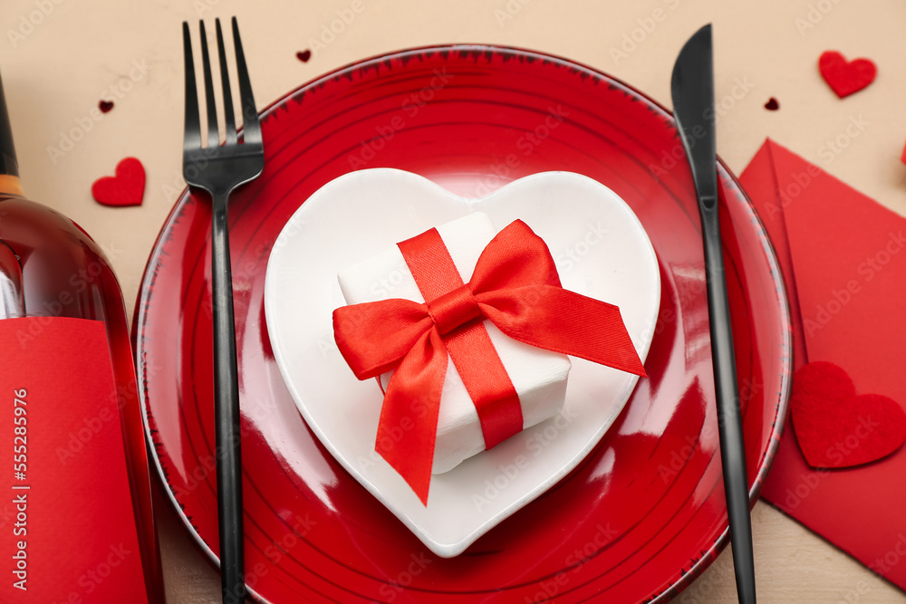 Table setting for Valentine's Day with gift and envelope on beige background, closeup