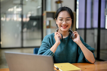 Wall Mural - Happy and charming young asian female college student looking at laptop screen, doing homework