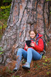 Smiling young female trekker reading a book under a tree in the forest.