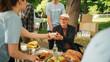 © Gorodenkoff - Group of Volunteers Helping in a Local Community Food Bank, Handing Out Free Food to People in Need in a Park on a Sunny Day. Man with Disabilities Using Wheelchair is Thankful for Charity Meal.