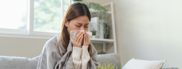 Wall Mural - Seasonal sick concept. the young woman has a common cold and sneezing on the sofa.