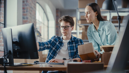 Wall Mural - Two Employees Preparing Orders Made from Online Sales in Their Internet Shop. Man and Female Working in a Storeroom. Young Man Using Desktop Computer, Woman Confirming Contact Details on Boxes.