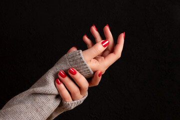 Wall Mural - Female hands in gray knitted sweater with beautiful manicure - red nails on dark black background. Nail care concept