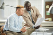 © Seventyfour - Side view portrait of two ethnic business executives reading documents while planning project in office