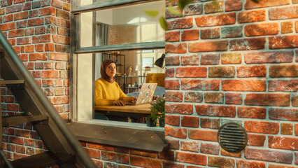 Poster - Portrait of a Young Muslim Female in a Hijab Sitting at a Desk, Working on Laptop Computer. Creative Freelance Writer Doing Remote Work from Home Office. Stylish Apartment Shot from Window.