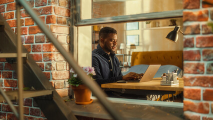 Aufkleber - Tired African Male Using Laptop at Home. Doing Remote Work During the Day. Frustrated Man Sitting at a Table, Working Long Hours on Computer, Brainstorming Creative Project. Outside the Window Shot.