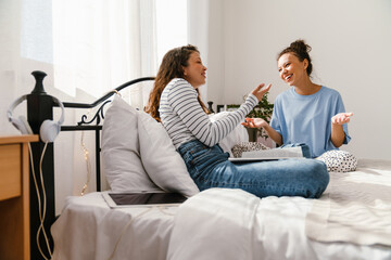 Young women laughing and chatting together while sitting in bed at home