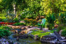 A Tranquil Stream Flows Through A Garden Area With A Green Adirondack Chair; Hudson, Quebec, Canada