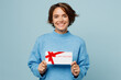 © ViDi Studio - Young cheerful happy smiling woman in knitted sweater hold gift certificate coupon voucher card for store isolated on plain pastel light blue cyan background studio portrait People lifestyle concept.