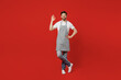 © ViDi Studio - Full body young housewife satisfied positive bachelor male housekeeper chef cook baker man wearing grey apron show ok okay gesture isolated on plain red color background studio. Cooking food concept.