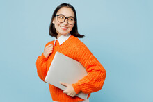 Side View Young Smiling Fun Smart IT Woman Of Asian Ethnicity Wear Orange Sweater Glasses Hold Closed Laptop Pc Computer Look Aside On Area Isolated On Plain Pastel Light Blue Cyan Background Studio.