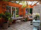 Fototapeta  - Interior of veranda. Cozy space in patio. A lot of plants. Orange wall. Wooden vintage furniture.