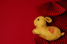 Golden Rabbit Over Red Background With Paper Fans. Text On Hare Means Wishing Of Fortune, Money, Prosperity. Lunar New Year Concept